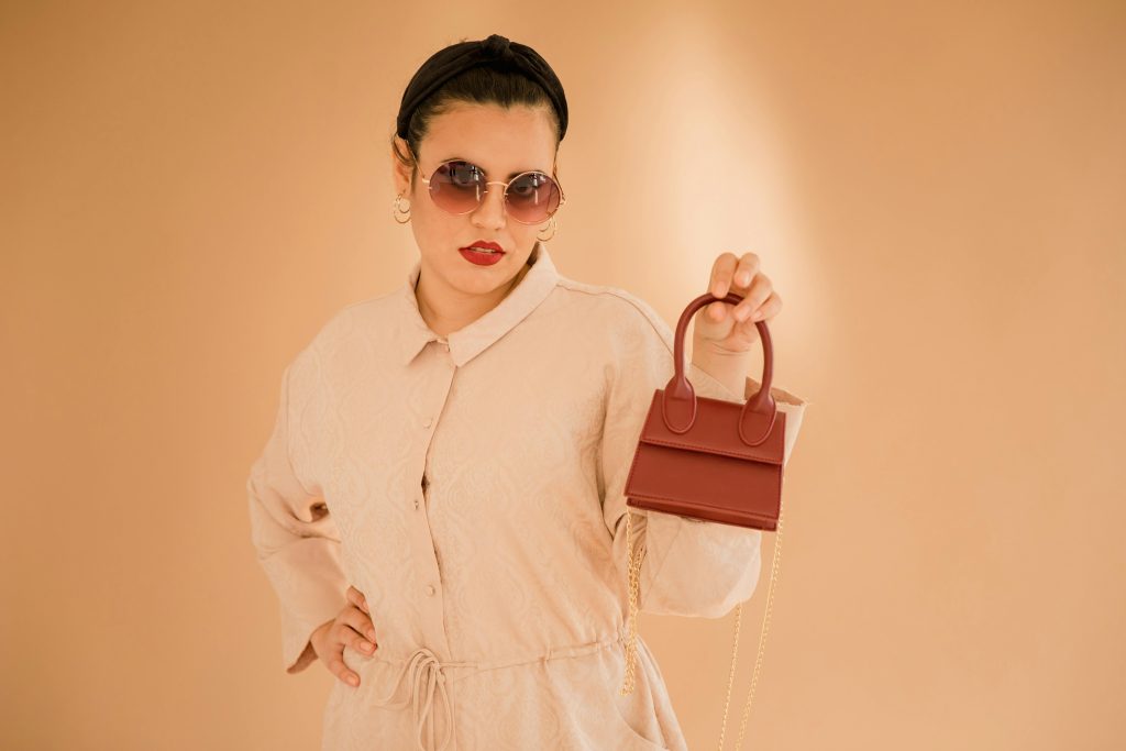 Fashionable woman in sunglasses holding a trendy mini bag in a studio setting.